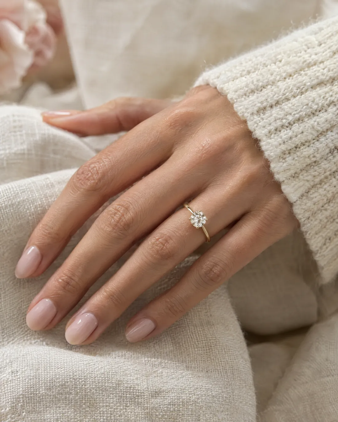 Hand mit Solitär-Verlobungsring in Gelbgold auf Leinen